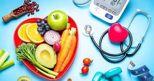 A picture of a heart shaped plate with veggies next to a stethescope, a blood pressure monitor, and hand weights. 